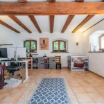 Das Bild zeigt ein helles Arbeitszimmer in einem Haus in Andechs-Frieding. Das Zimmer hat freiliegende dunkle Holzbalken und helle Wände. Ein großer Schreibtisch mit Computer, eine braune Ledercouch und viele Regale mit Büchern sind zu sehen.