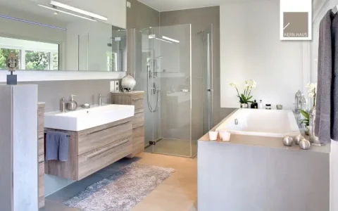 Modernes Badezimmer: Holzwaschtisch mit Aufsatzbecken, große Spiegel, Glasduschabtrennung, eingelassene Badewanne, graue Fliesen. Deko: Kerzen, Pflanzen, Handtücher. Leuchten im Spiegel integriert.