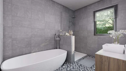 Das Bild zeigt ein modernes Badezimmer in neutralen Grautönen. Zu sehen sind eine freistehende weiße Badewanne, eine Dusche mit Glaswand sowie eine Fensterfront, die Ausblick auf grünes Geäst bietet. Ein Waschtisch mit weißen Blumen vervollständigt den Raum.