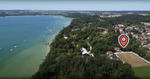Luftaufnahme eines Baugrundstücks in Inning am See. Gezeigt sind ein See mit vielen Booten, umliegende Dächer der Ortsbebauung und Felder. Markierter Punkt könnte Ziel für Immobilienerwerb sein.
