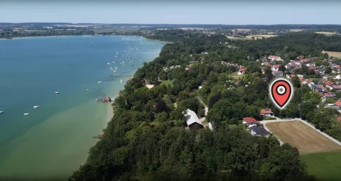 Luftaufnahme eines Baugrundstücks in Inning am See. Gezeigt sind ein See mit vielen Booten, umliegende Dächer der Ortsbebauung und Felder. Markierter Punkt könnte Ziel für Immobilienerwerb sein.
