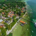 Luftbild von Schondorf am Ammersee zeigt einen Dampfer am Dampfersteg. Umliegend Segelboote, dichte Bebauung mit roten und grauen Dächern, grüne Uferzonen und Waldstücke.