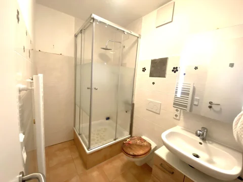 Modernes Duschbad: Eleganz und Funktionalität kombiniert Das Bild zeigt ein modernes Badezimmer mit einer Duschkabine, einem Waschbecken und einem Handtuchhalter. Die Duschkabine ist aus Glas und die Fliesen sind weiß mit dekorativen, blauen Mustern.