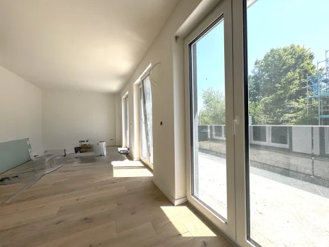 Das Bild zeigt einen hellen Essbereich mit Parkettboden und drei großen Fensterelementen, die viel Licht hereinlassen. An der Seite steht Baumaterial, was darauf hindeutet, dass der Raum vor kurzem renoviert wurde.