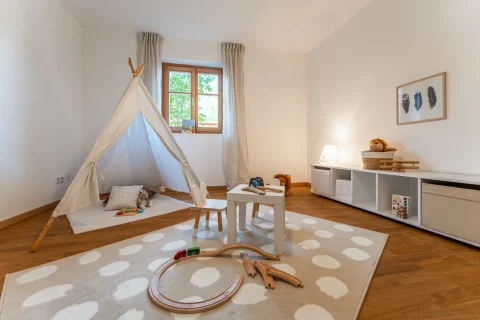 Kinderzimmer in einer Ferienwohnung mit Tipi-Zelt, Spielteppich, Aufbewahrungsmöbel und Fensterblick. Ideal zum Kaufen am Schliersee für Familien.