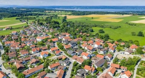 Luftaufnahme von Frieding, zeigt eine dicht bebaute Wohnsiedlung mit vielen Einfamilienhäusern und umgebenden Grünflächen und Feldern. Die Anordnung der Häuser ist organisiert, umgeben von Straßen und Bäumen.