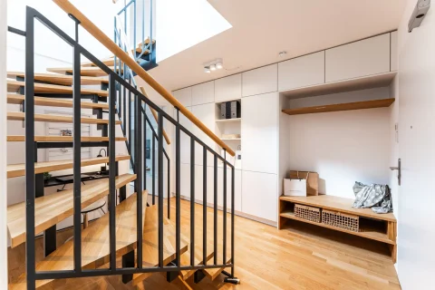 Moderne Einrichtung mit stilvoller Garderobe und Treppe Moderne Eingangshalle mit Holztreppe, schwarzem Metallgeländer, einer eingebauten weißen Schrankwand und einer Garderobe rechts, bestehend aus Holzbänken und Fächern. Ein lichtdurchfluteter Raum mit Holzboden.