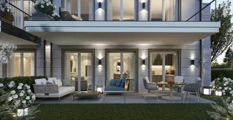 Das Bild zeigt eine moderne Gartenansicht eines zweistöckigen Hauses bei Abenddämmerung. Im Vordergrund ist ein gepflegter Rasen mit Blumenbeeten und Gartenmöbeln zu sehen. Spotlights beleuchten die Fassade stilvoll.