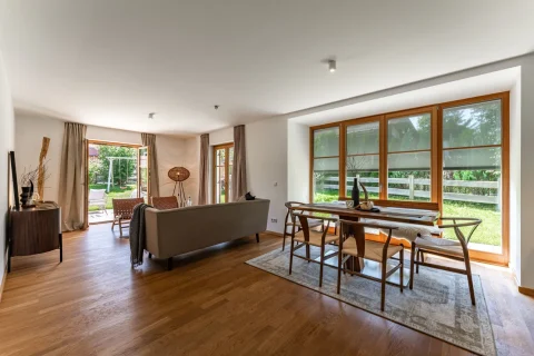 Helles, geräumiges Wohnzimmer in einer Wohnung in Schliersee. Große Fensterfront mit Blick auf den Garten, moderne Einrichtung mit Holzakzenten und eine bequeme Sitzgruppe.