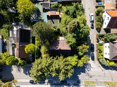 Luftaufnahme einer Straße mit einzelnen Häusern und einem freien Grundstück, möglicherweise in München. Dichte Begrünung umgibt die Gebäude und Autos parken am Straßenrand. Ideal für 