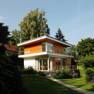 Modernes Einfamilienhaus mit großzügigen Fensterfronten und Holzverkleidung. Umgeben von einem gepflegten Garten, umrahmt von hohen Bäumen. Ideal für Immobiliensuchende am Ammersee und Wörthsee.