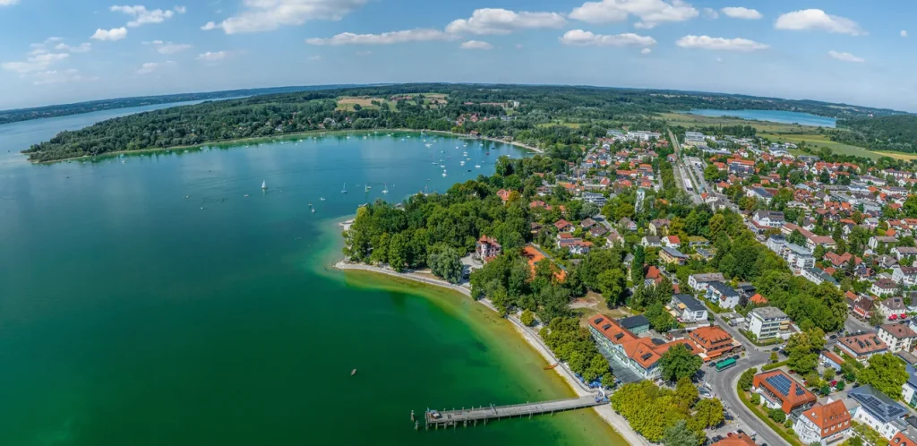 Luftaufnahme von Herrsching am Ammersee zeigt dicht bebaute Wohngegenden, grüne Flächen und den klaren Ammersee mit Booten. Ideal für Immobilienmakler, die in attraktiven Lagen vermitteln wollen.