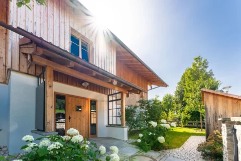 Einladendes Einfamilienhaus mit schlichtem Charme in Schliersee. Die Holzfassade kombiniert rustikales und modernes Design neben einem Garten mit Hortensien. Ideal für Immobilienmakler, die Wohnungen in naturnahen Lagen anbieten.