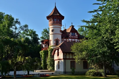 Malerisches Kurparkschlösschen in Herrsching am Ammersee Das Bild zeigt das Kurparkschlösschen in Herrsching am Ammersee, ein malerisches Bauwerk im Fachwerkstil mit einem markanten Turm, umgeben von üppigem Grün und einem gepflegten Garten.