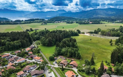 Luftbild Lage Das Luftbild zeigt eine ländliche Region am Tegernsee mit einer Siedlung von Häusern, umgeben von Wäldern und Feldern. Im Hintergrund sind Berge und der teilweise sichtbare Tegernsee zu erkennen.
