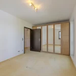 Das Bild zeigt einen leeren Raum mit hellen Wänden, einem Holzboden und Wandschränken aus hellem Holz. An der Decke befinden sich Spots. Zwei Türen, eine dunkle Eingangstür und eine Innentür, führen hinein.