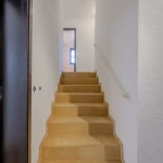 Das Bild zeigt eine moderne Treppe in einem Innenraum. Eine Holztür ist links geöffnet, und die Treppe aus hellem Holz führt nach oben zu einem weiteren Stockwerk. Es handelt sich vermutlich um einen renovierten Altbau, basierend auf den Adressdaten "München Oldenbourgstraße 13a".