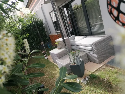 Terrasse mit grauer Rattan-Lounge, Kissen, Beistelltischen, Pflanzenkübeln und Markise vor Schiebetüren und kleinem Rasen