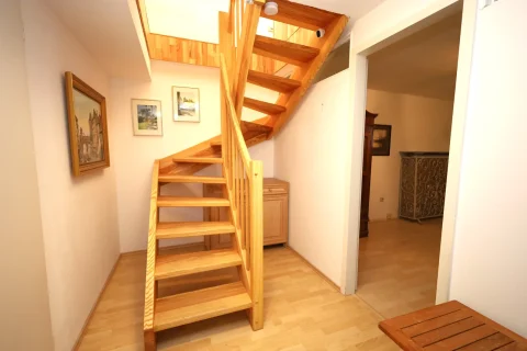 Holztreppen in einem Innenraum führen vermutlich in den Keller oder Hobbyraum. An der Wand hängen Bilder. Rechts im Hintergrund ist ein Eingang zu einem weiteren Raum. Links unten steht ein kleiner Holzhocker.