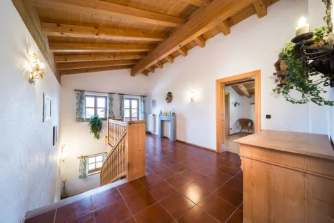 Treppenhaus Helles Treppenhaus mit holzvertäfeltem Dach und braun gefliestem Boden. Eine hölzerne Geländer und Treppen führen hinunter. Wände mit Dekorationen, ein Kronleuchter und eine offene Tür führen in ein weiteres Zimmer.