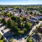 Luftaufnahme von Obersendling, München. Gezeigt wird eine ruhige Wohngegend mit Einfamilienhäusern, Gärten und gepflasterten Straßen. Im Hintergrund zeichnen sich Berge ab, was typisch für die Region ist.